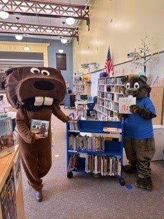 people in beaver costumes holding books in a library